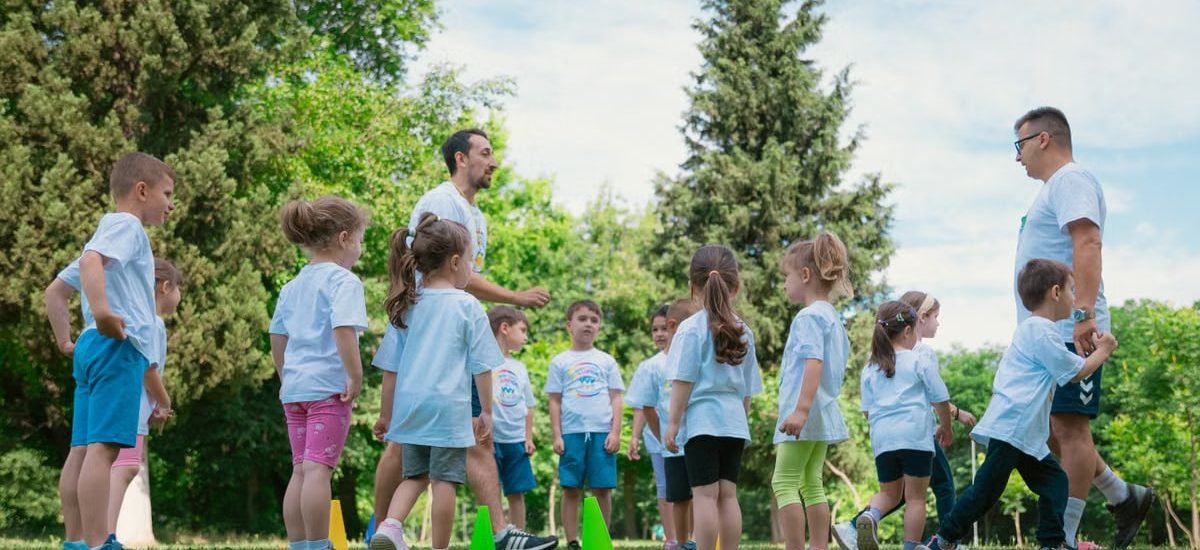Group of children and teachers playing and learning in a sunny park setting.