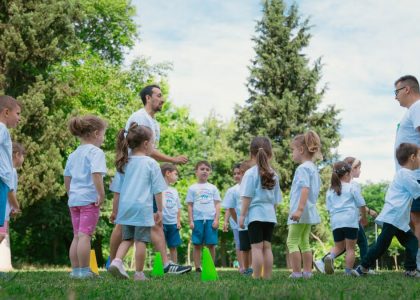 Group of children and teachers playing and learning in a sunny park setting.